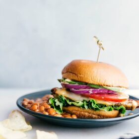 A chicken burger on a plate accompanied by a side of baked beans, presenting a delicious and satisfying meal, ready for enjoyment.