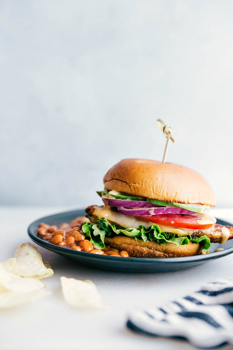 A chicken burger on a plate accompanied by a side of baked beans, presenting a delicious and satisfying meal, ready for enjoyment.