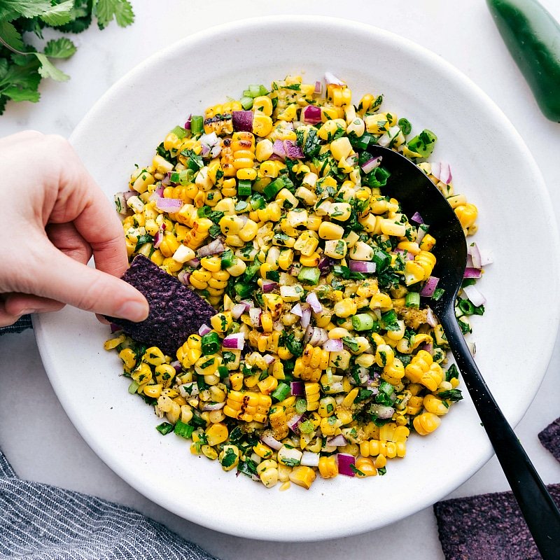 Finished and delicious corn salsa with a chip being dipped into it, showcasing a perfect blend of flavors.