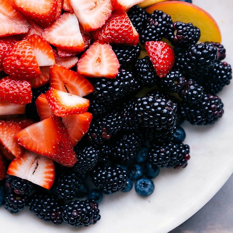 Freshly cut strawberries, blackberries, blueberries, and peaches, neatly arranged and ready to be used in the delicious fruit salad recipe.