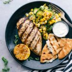 A plate featuring Greek chicken served with naan bread and a zucchini and corn salad, offering a delicious and flavor-packed meal.
