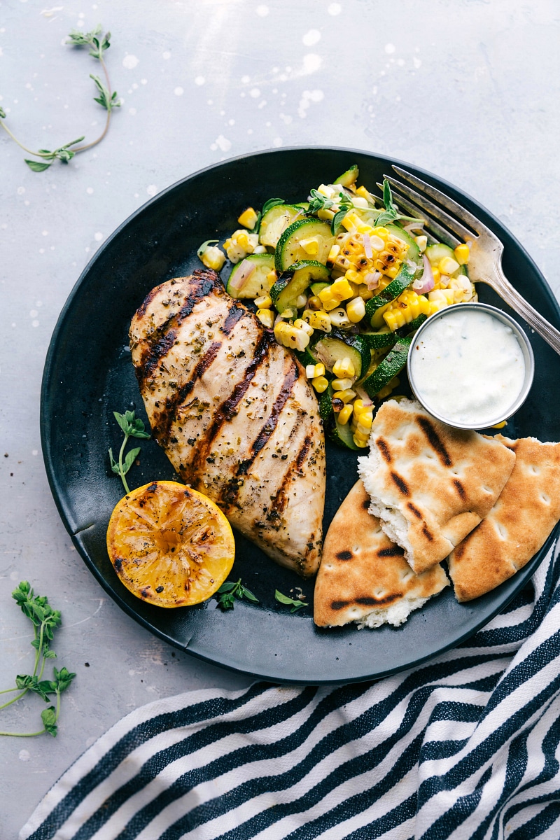 Overhead view of Greek Chicken on a plate with the naan bread, chicken, and zucchini and corn salad.