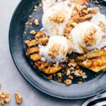 A delightful twist on a classic sundae, featuring grilled pineapple topped with vanilla ice cream and sprinkled nuts, combining warm and cold elements for a unique dessert experience.