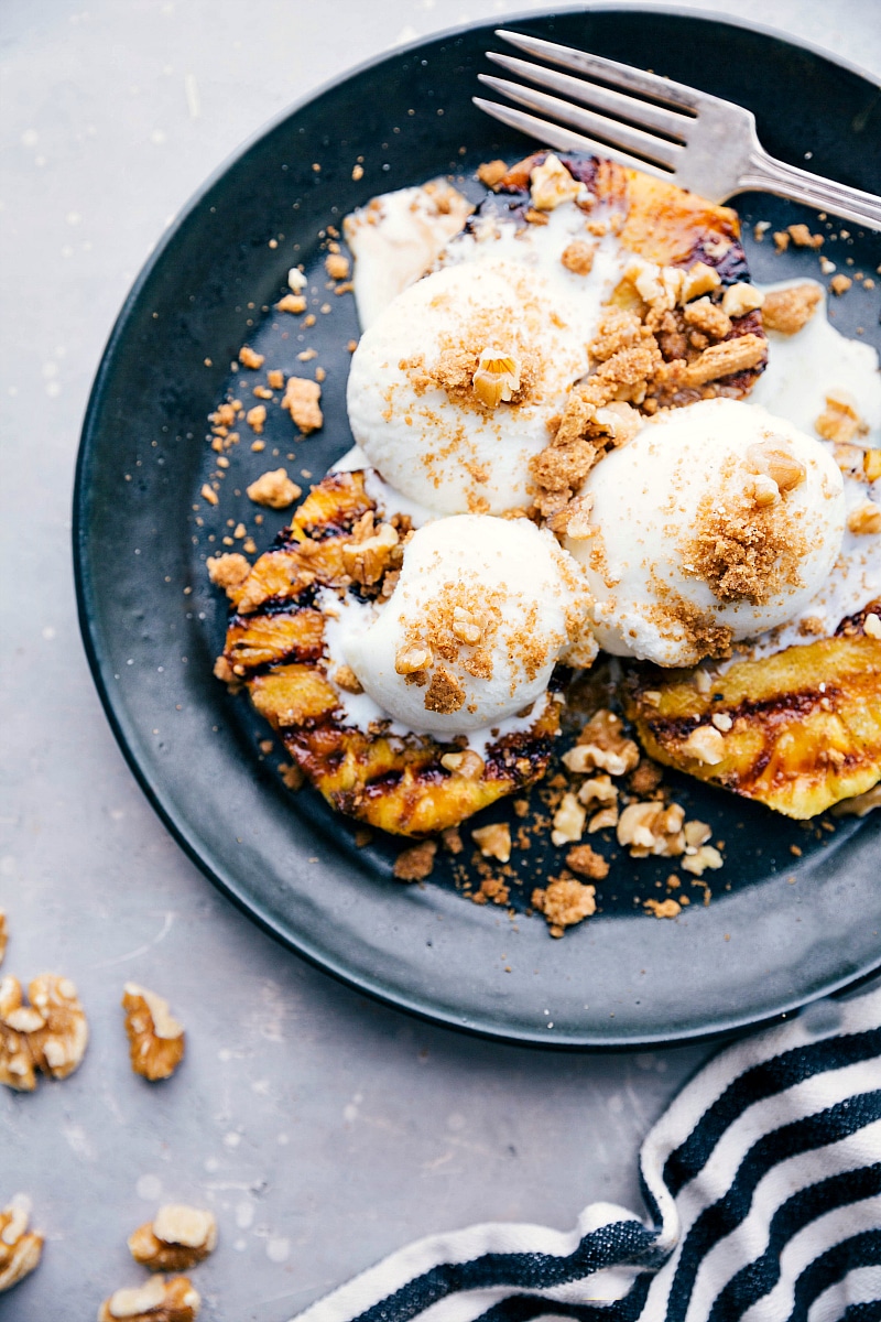 A delightful twist on a classic sundae, featuring grilled pineapple topped with vanilla ice cream and sprinkled nuts, combining warm and cold elements for a unique dessert experience.