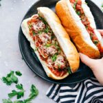 A plate filled with mouthwatering meatball subs, where the buns are overflowing with meat and flavor, topped with cheese and fresh herbs, all set for a delightful meal.
