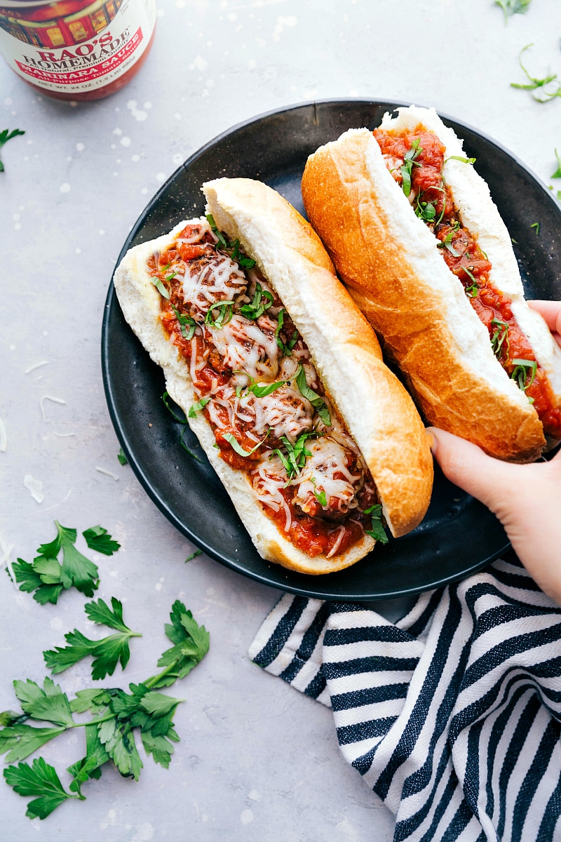 A plate filled with mouthwatering meatball subs, where the buns are overflowing with meat and flavor, topped with cheese and fresh herbs, all set for a delightful meal.