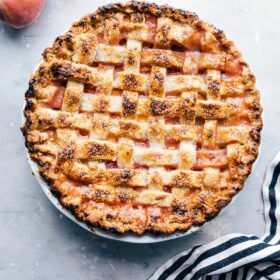 Delicious and sweet peach pie, fresh out of the oven and topped with sugar, accompanied by fresh peaches on the side.
