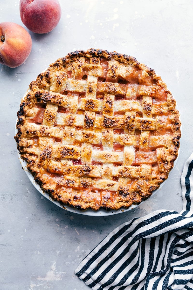 Delicious and sweet peach pie, fresh out of the oven and topped with sugar, accompanied by fresh peaches on the side.