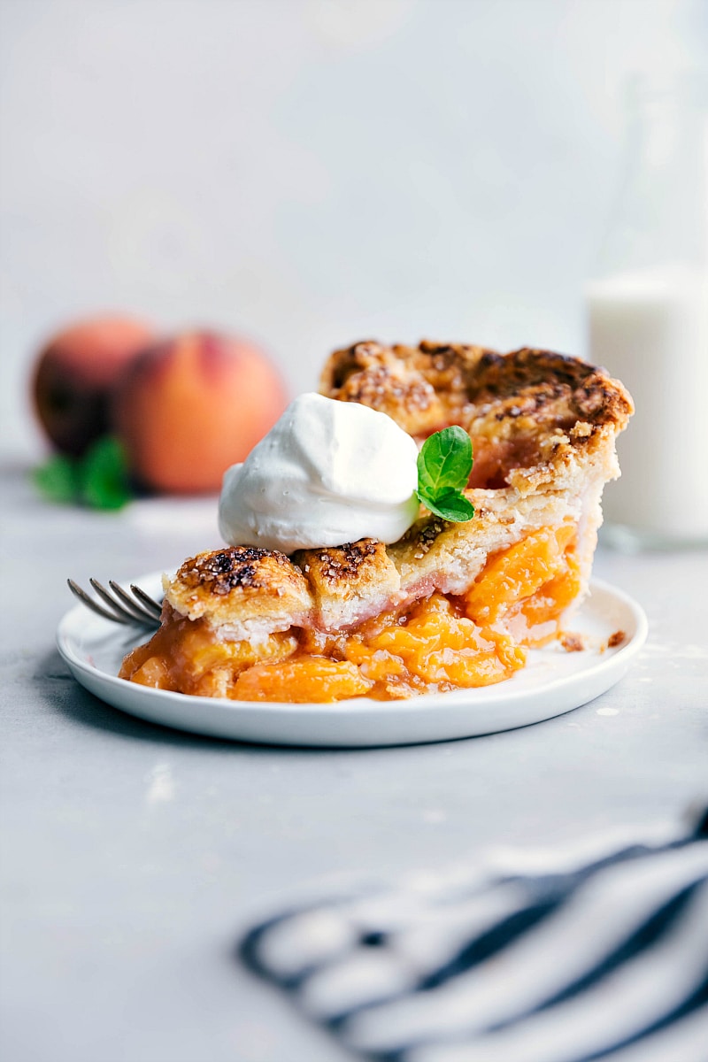A slice of the finished fresh peach pie recipe, revealing the warm and gooey interior, topped with a dollop of whipped cream, ready to be savored.