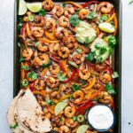 Freshly baked shrimp fajitas on a sheet pan, accompanied by tortillas and a variety of toppings, all set for assembly into a mouthwatering and savory meal.