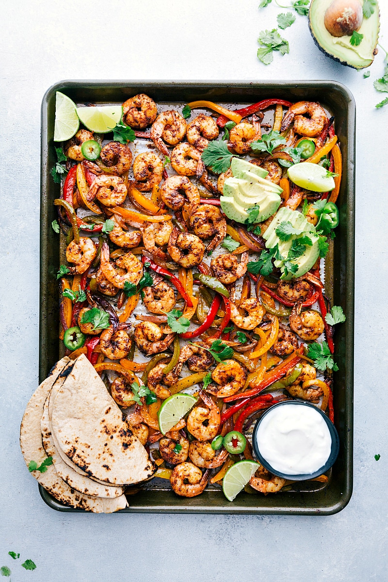 Overhead image of Shrimp Fajitas, fresh out of the oven, on a sheet pan with the tortillas and other toppings