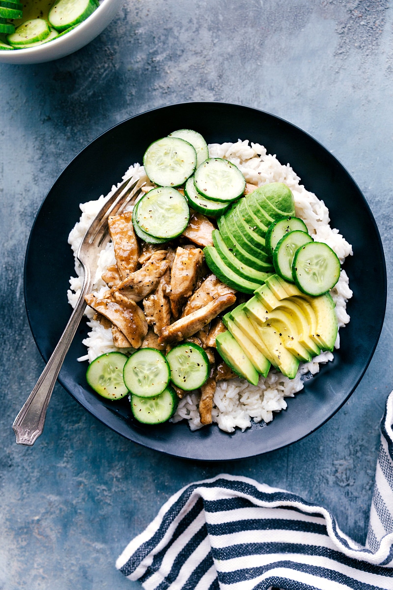 Overhead image of Apricot Chicken in a bowl with rice, avocado, and cucumbers.