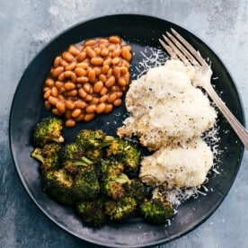 Baked alfredo chicken served on a plate with beans and baked broccoli.
