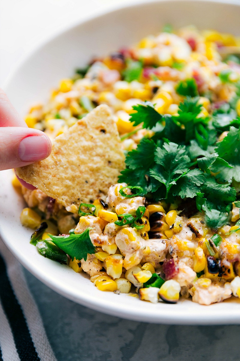 A chip being dipped into the creamy Mexican corn salad, scooping up a perfect savory bite.