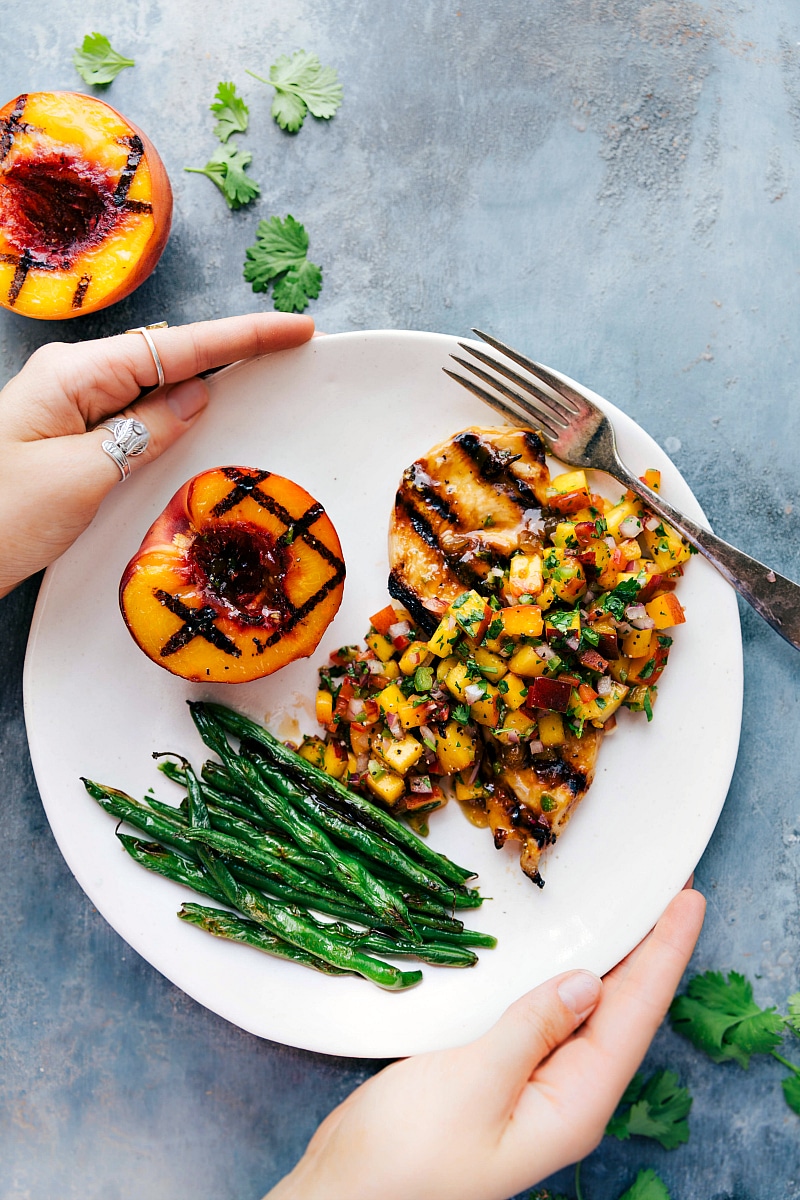 Overhead image of Peach Salsa Chicken, on a plate with green beans and a freshly grilled peach on the side.