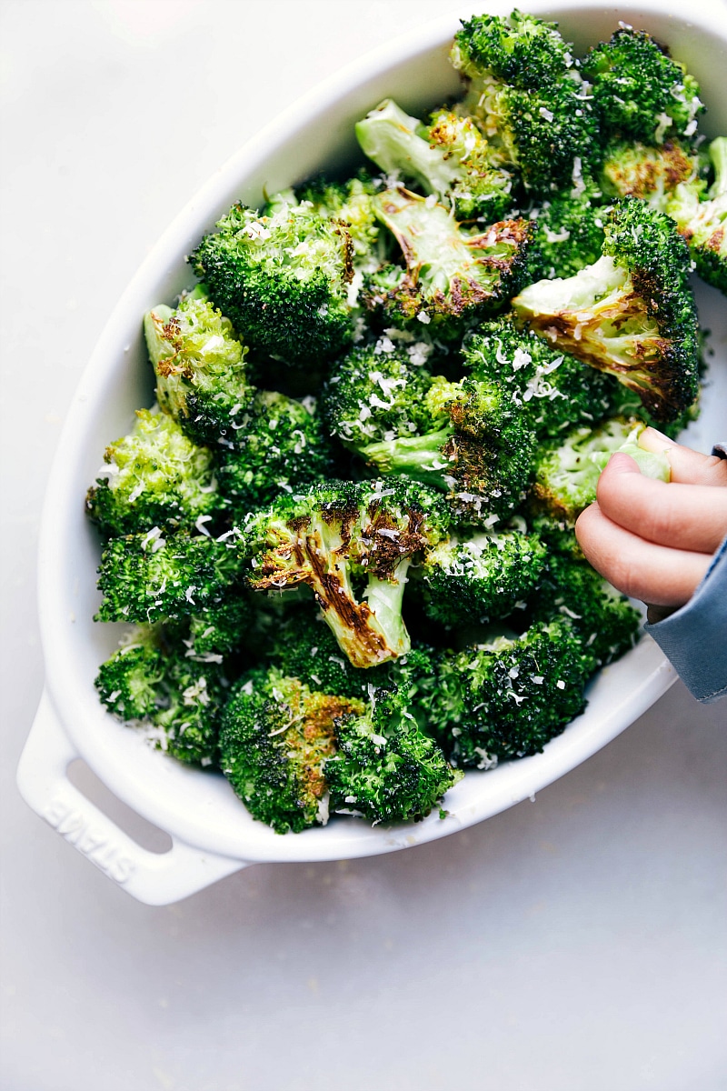 End shot of roasted broccoli with a child grabbing broccoli out of the dish