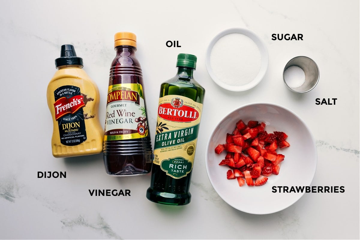 All the ingredients in this recipe prepped and ready to go, including strawberries, sugar, salt, oil, red wine vinegar, and Dijon.