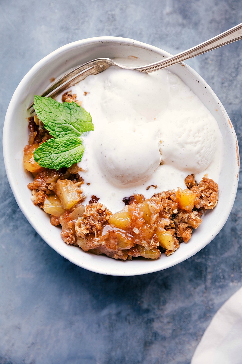 Overhead image of Apple Crumble in a bowl ready to eat, with ice cream on top, fresh mint, and a fork on the side.