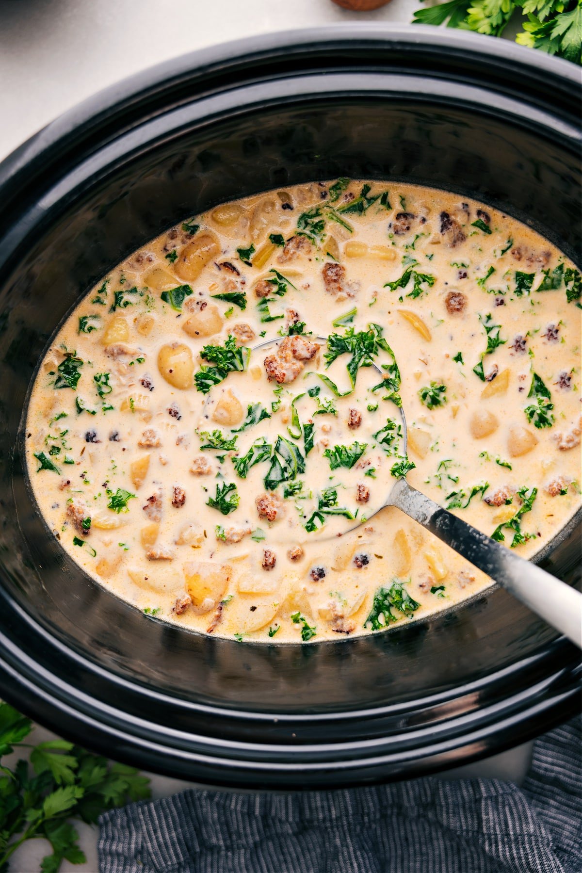 Bowl of Hearty and Warm Zuppa Toscana Soup Zuppa Toscana Soup simmering in the crockpot while a ladle scoops it up.