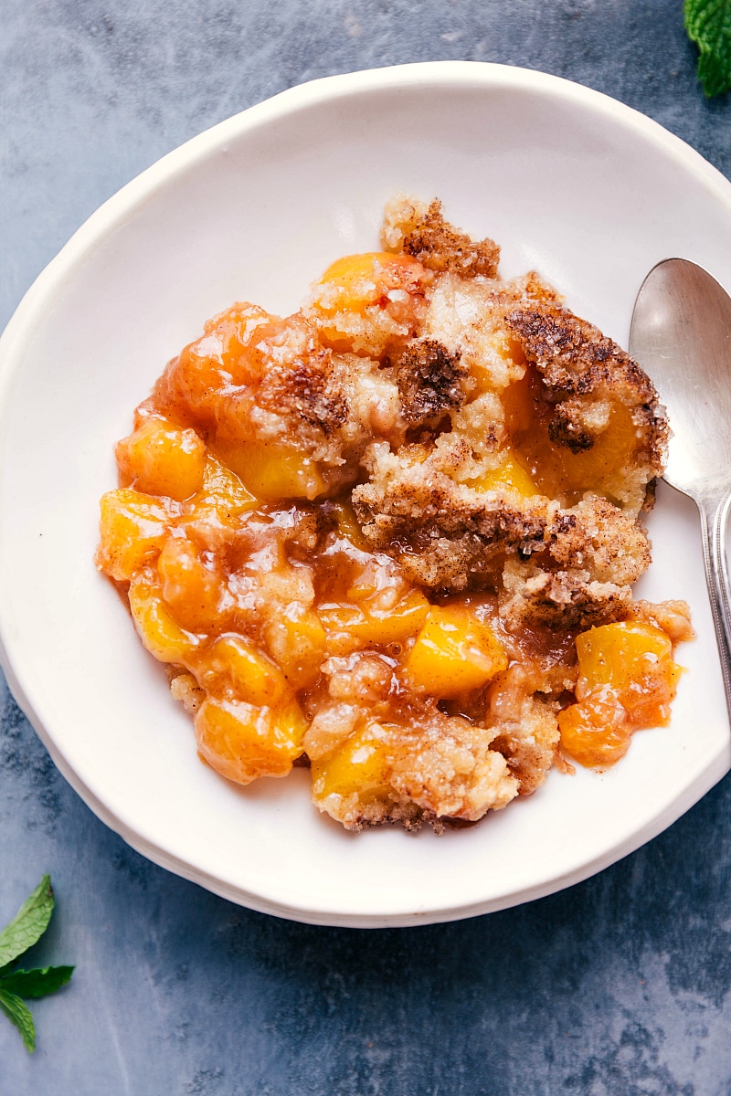 Overhead image of the Peach Cobbler in a bowl with a spoon on the side, ready to be eaten.