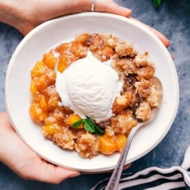 Sweet and delicious peach cobbler in a bowl with a scoop of vanilla ice cream on top.