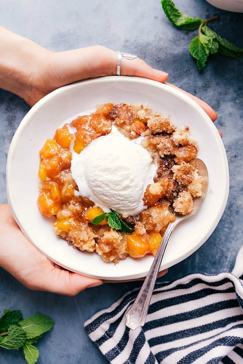 Sweet and delicious peach cobbler in a bowl with a scoop of vanilla ice cream on top.