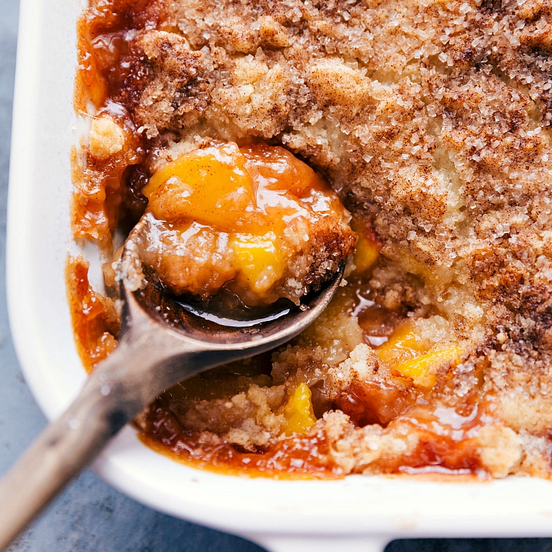 Up-close image of a spoonful of peach cobbler being scooped out of the casserole dish.