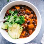 Sweet potato black bean chili served in a bowl, topped with sliced avocados and fresh cilantro, making for a warm and delicious meal.