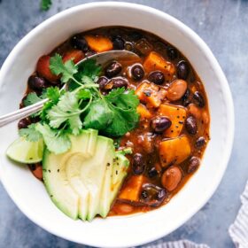 Sweet potato black bean chili served in a bowl, topped with sliced avocados and fresh cilantro, making for a warm and delicious meal.