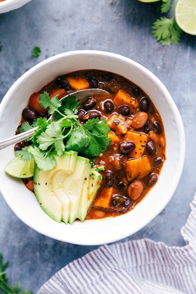 Sweet potato black bean chili served in a bowl, topped with sliced avocados and fresh cilantro, making for a warm and delicious meal.