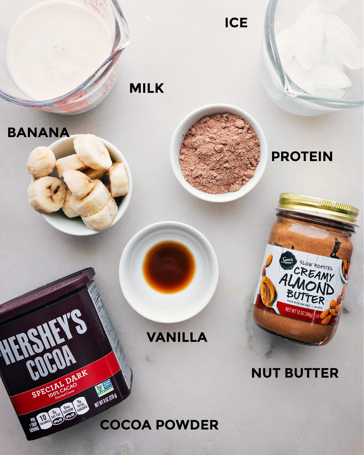 All the ingredients including milk, ice, cocoa powder, nut butter, vanilla, and protein powder prepped out for easy assembly.