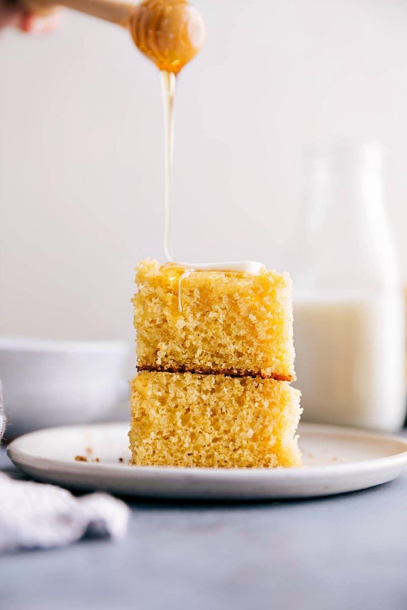 Image of two slices of Cornbread stacked on top of each other with honey being poured on top.