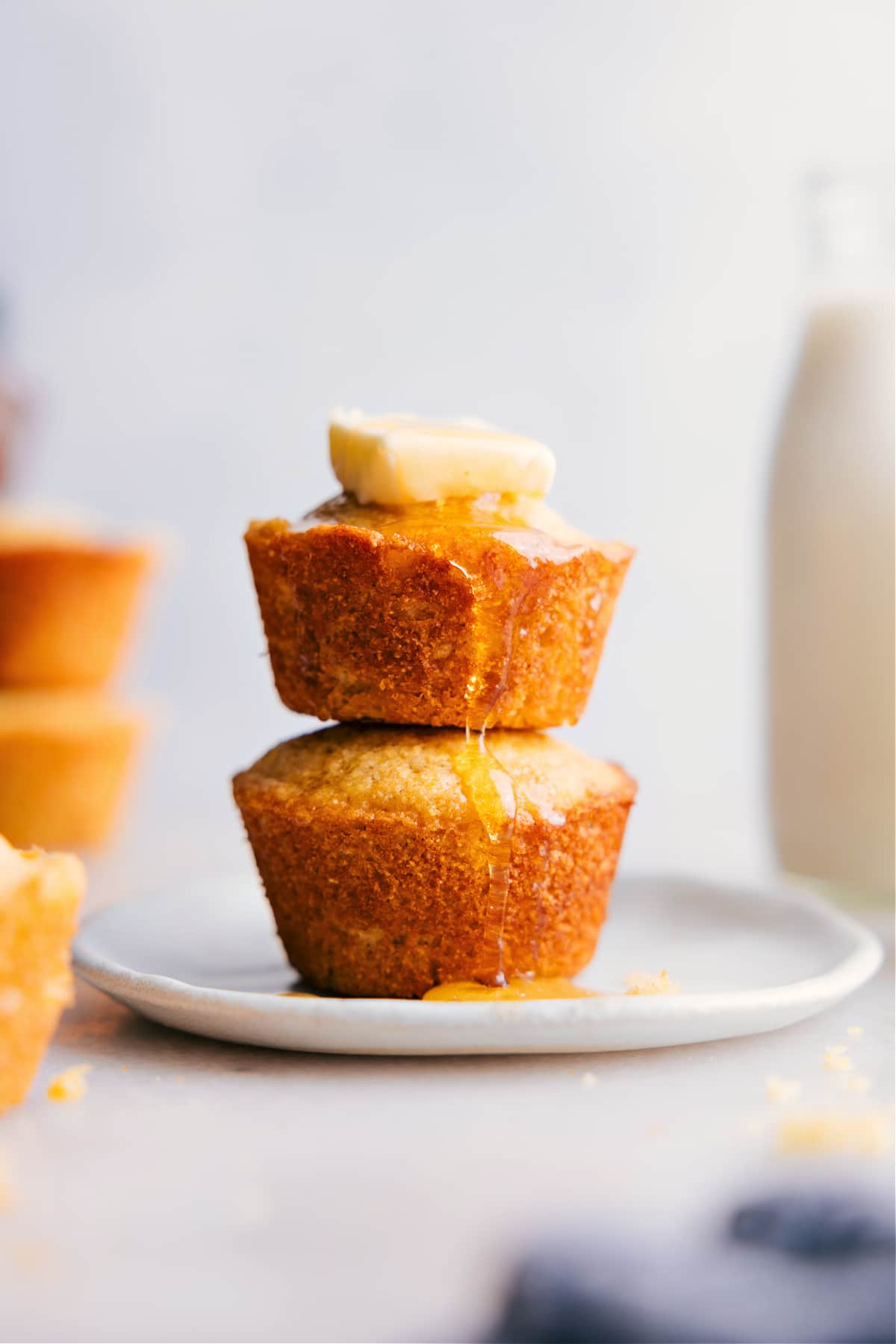 Finished cornbread muffins stacked on top of each other, with honey and butter melting on top, ready to be enjoyed.