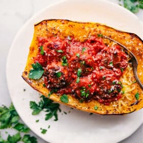 Finished spaghetti squash filled with marinara and meatballs, topped with fresh cheese and herbs.