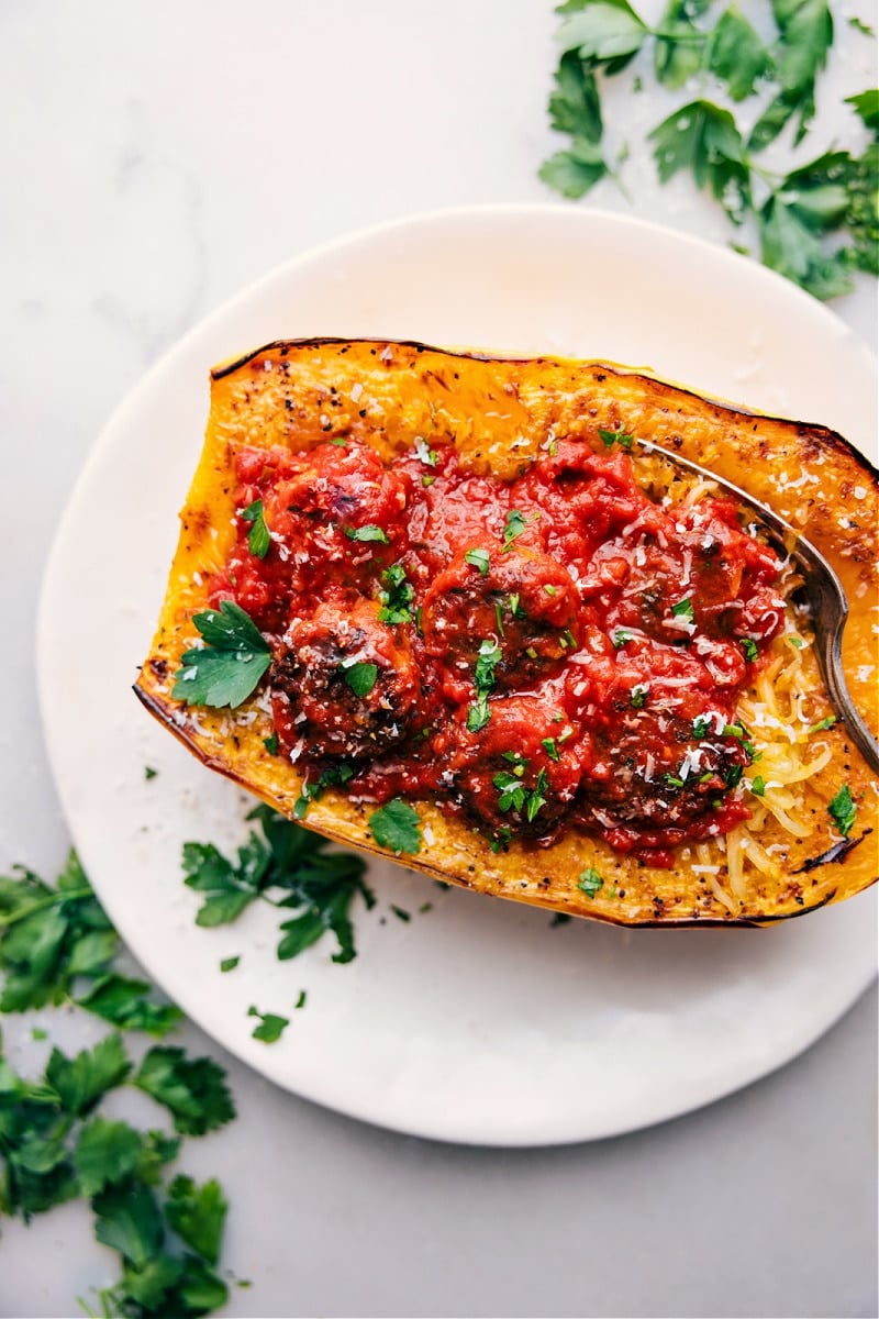 Finished spaghetti squash filled with marinara and meatballs, topped with fresh cheese and herbs.