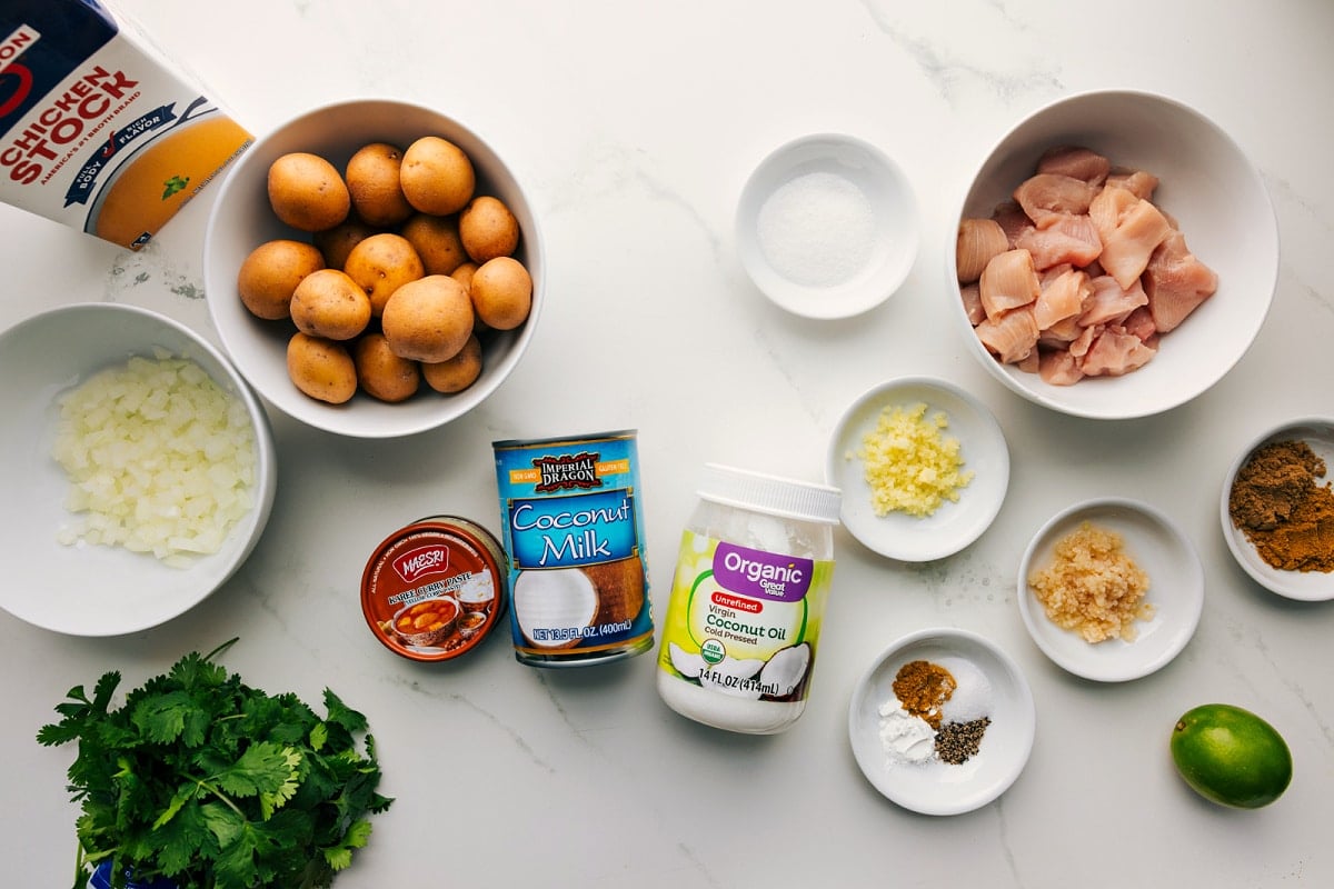 All the ingredients in this recipe prepped out for easy assembly including the stock, onions, cilantro, curry paste, coconut milk, coconut oil, spices, garlic, ginger, lime, chicken, potatoes, and sugar.