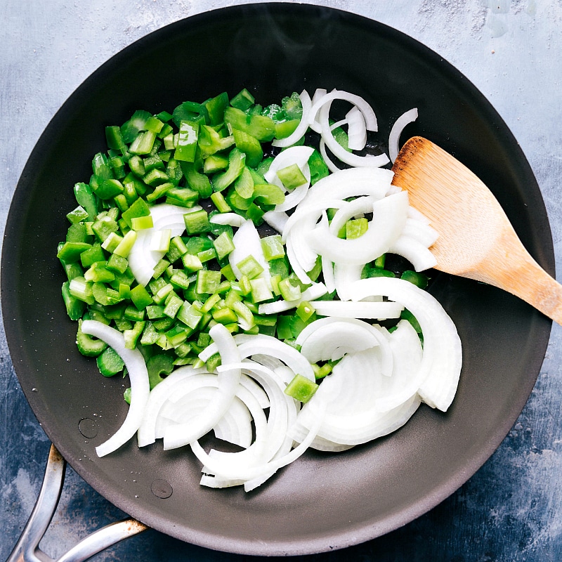 Fresh peppers and onions being sautéed in a pan.