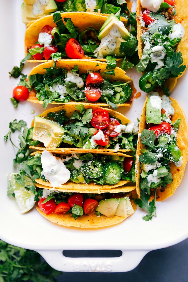 Baked chicken tacos fresh out of the oven, topped with fresh vegetables, herbs, and a delicious sauce.
