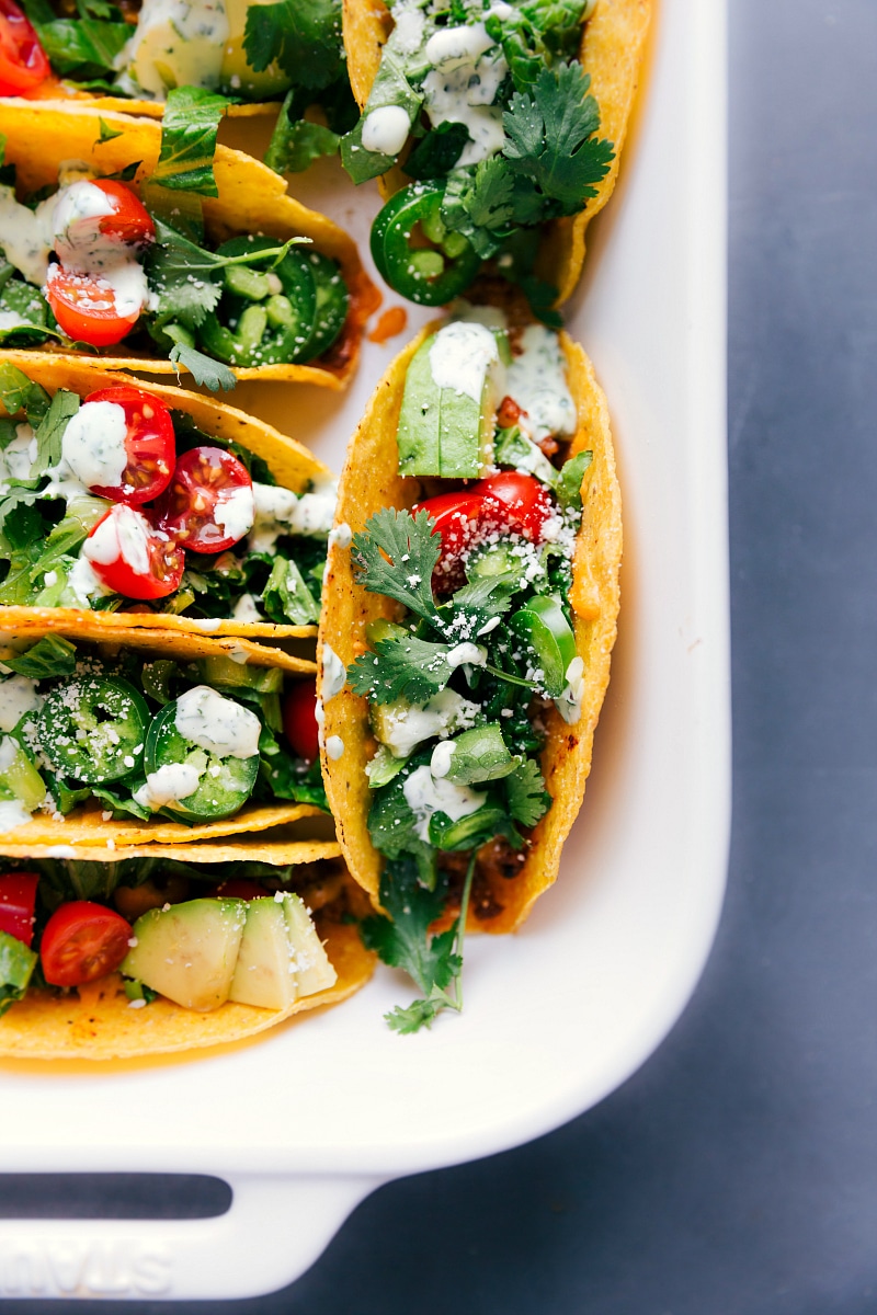 Baked chicken tacos in a casserole dish, filled with seasoned meat, melted cheese, fresh vegetables, and bursting with flavor.