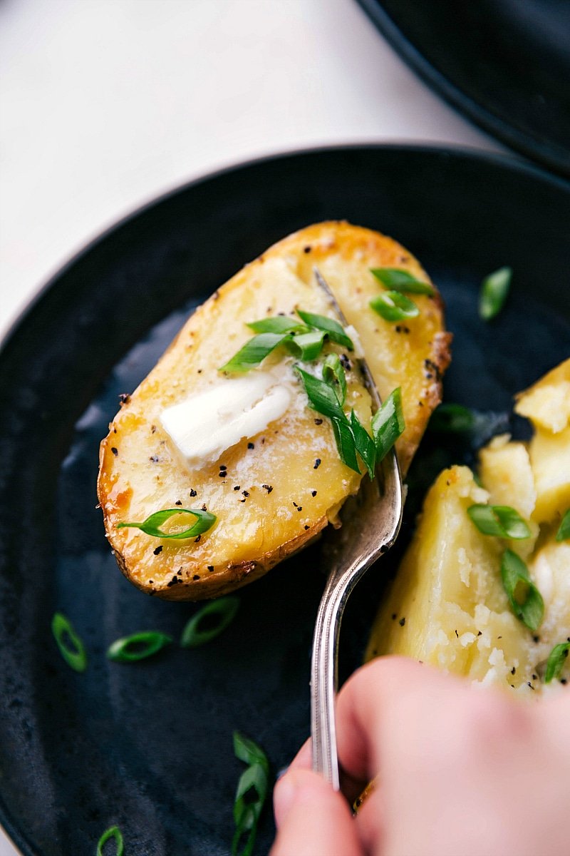 Overhead image of Baked Potatoes being eaten with butter and fresh chives on top.