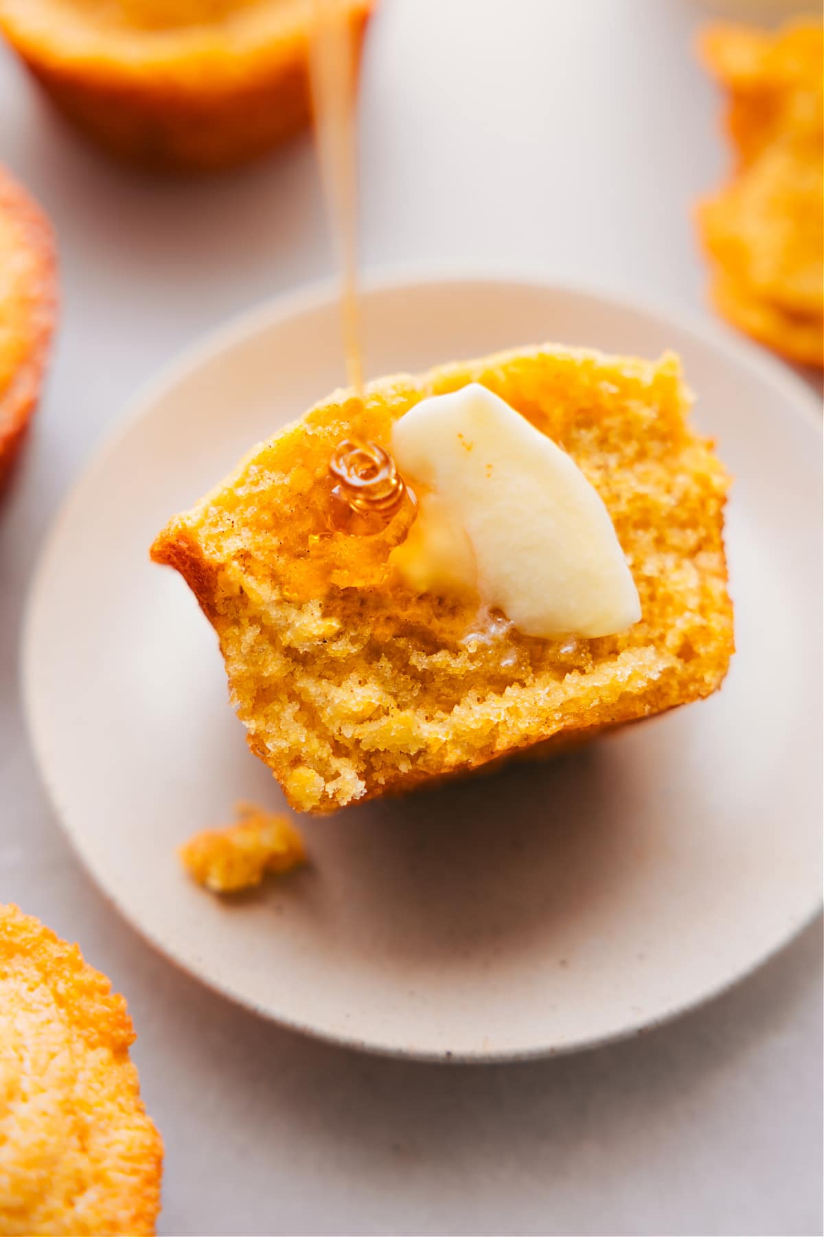 Freshly baked cornbread muffin, cut in half to reveal its fluffy interior, served with butter and honey on top.