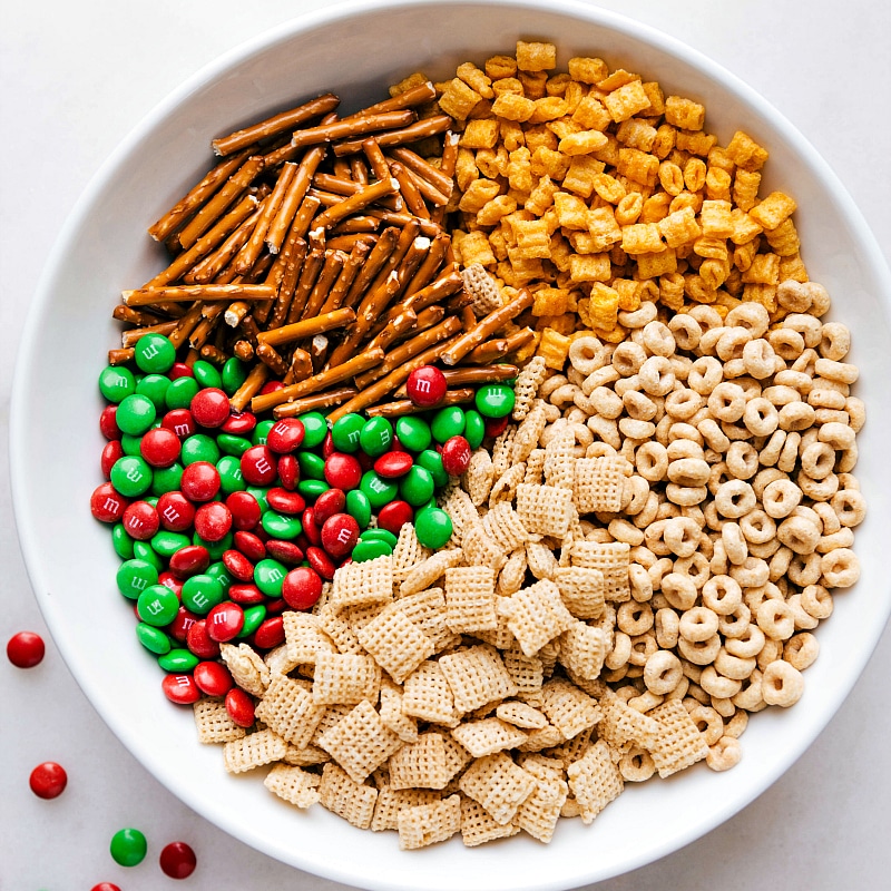 Ingredients for Christmas snack mix recipe displayed, including pretzels, chex cereal, cheerios, and more.