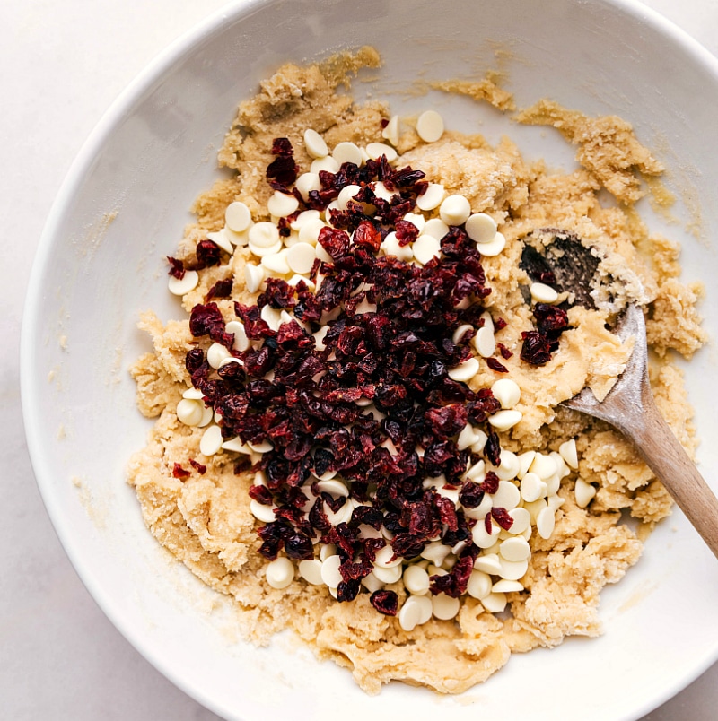 White chocolate chips and cranberries being added to cookie dough, enhancing the flavors for a delightful taste combination.