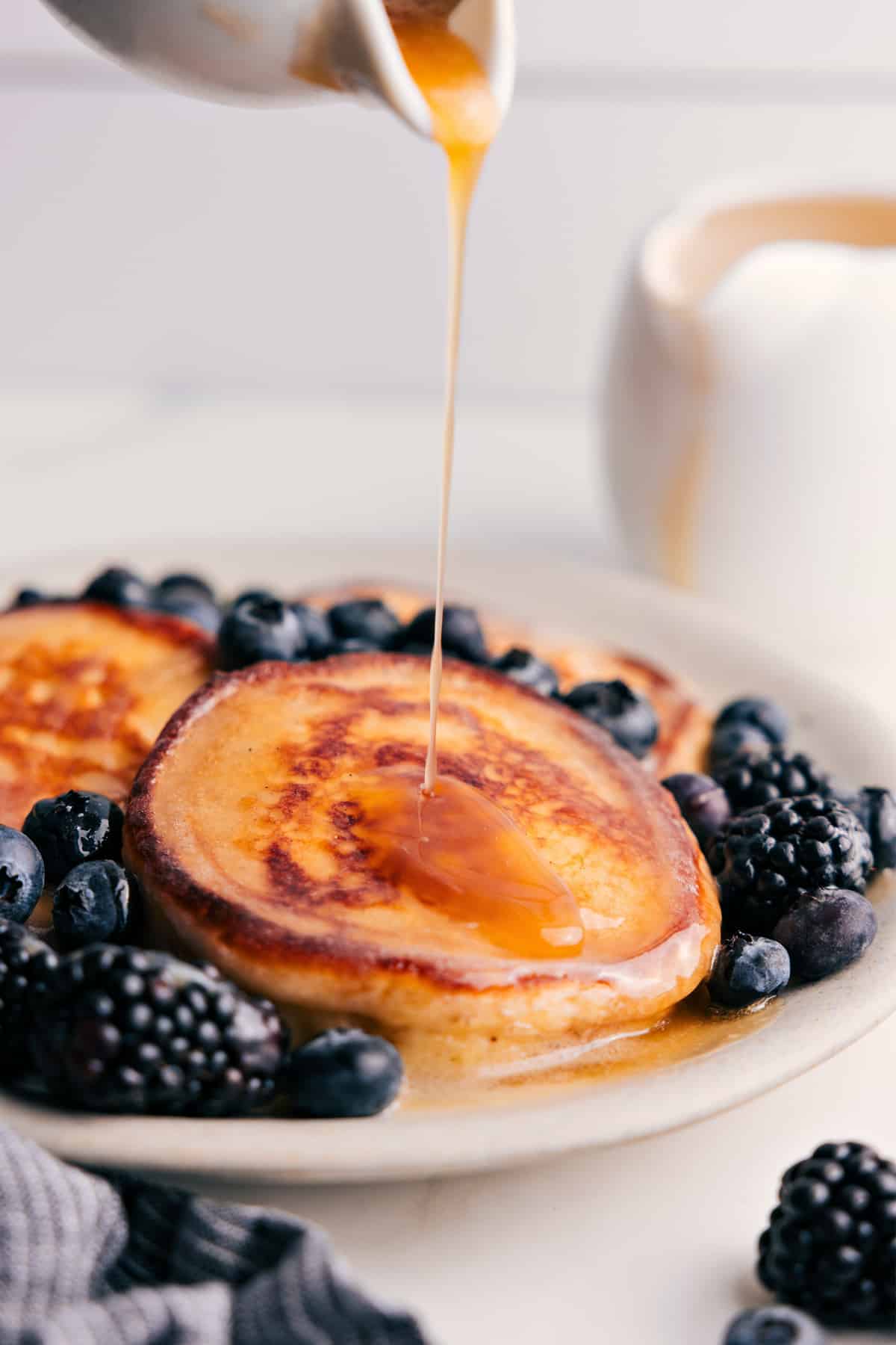 The syrup being drizzled over a plate of pancakes.