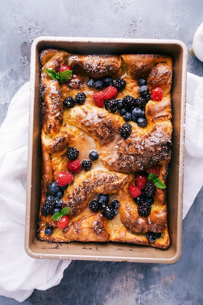 Dutch baby pancake freshly baked, topped with an array of fresh fruit and drizzled with syrup.