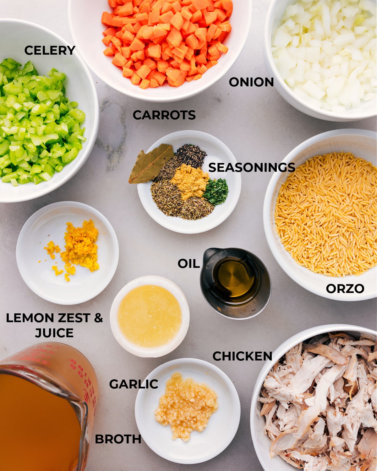 Assorted fresh ingredients for lemon orzo chicken soup displayed, including lemon, chicken, orzo pasta, vegetables, and herbs.