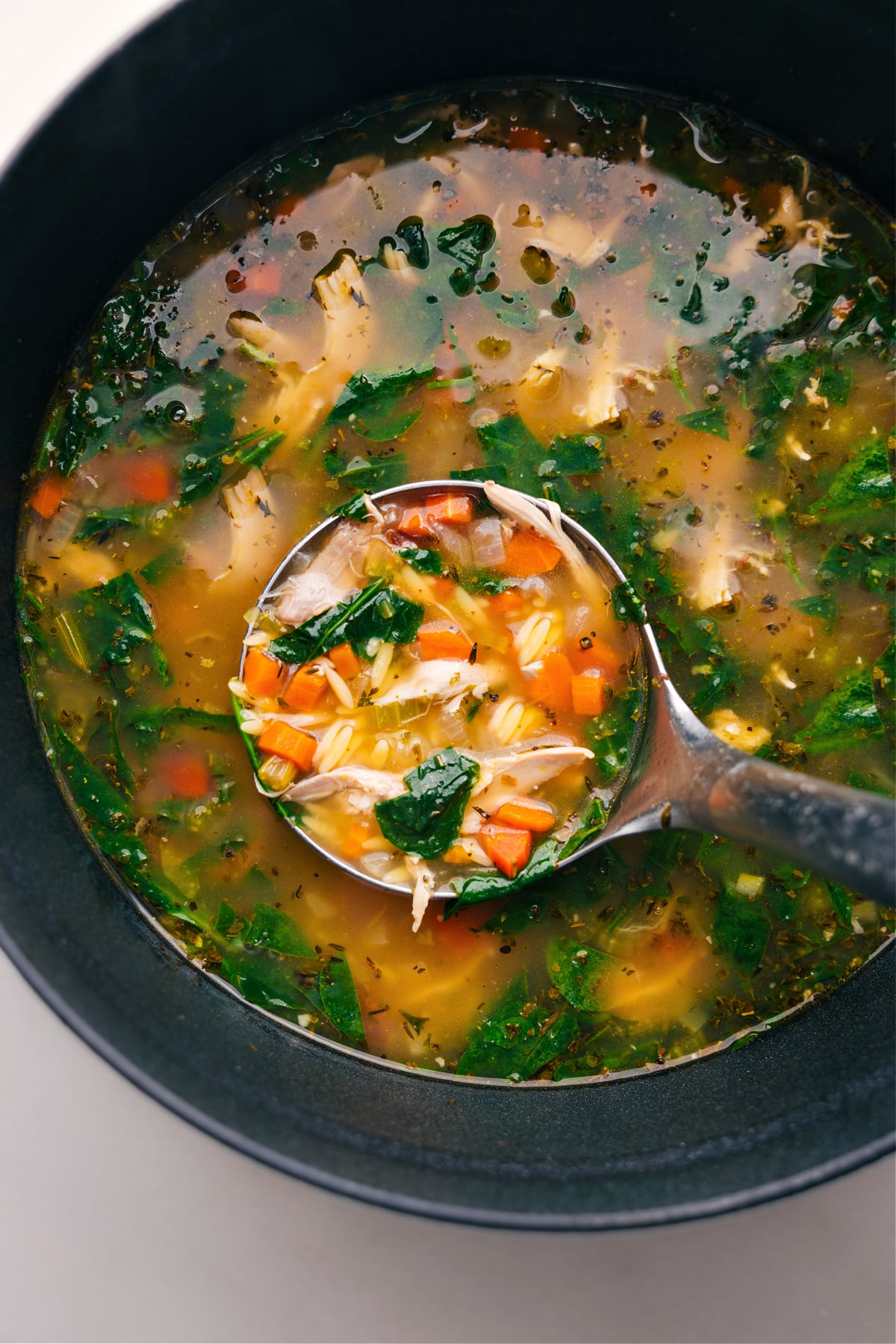 Steaming lemon chicken orzo soup in a pot, with a ladle serving a portion rich with ingredients.
