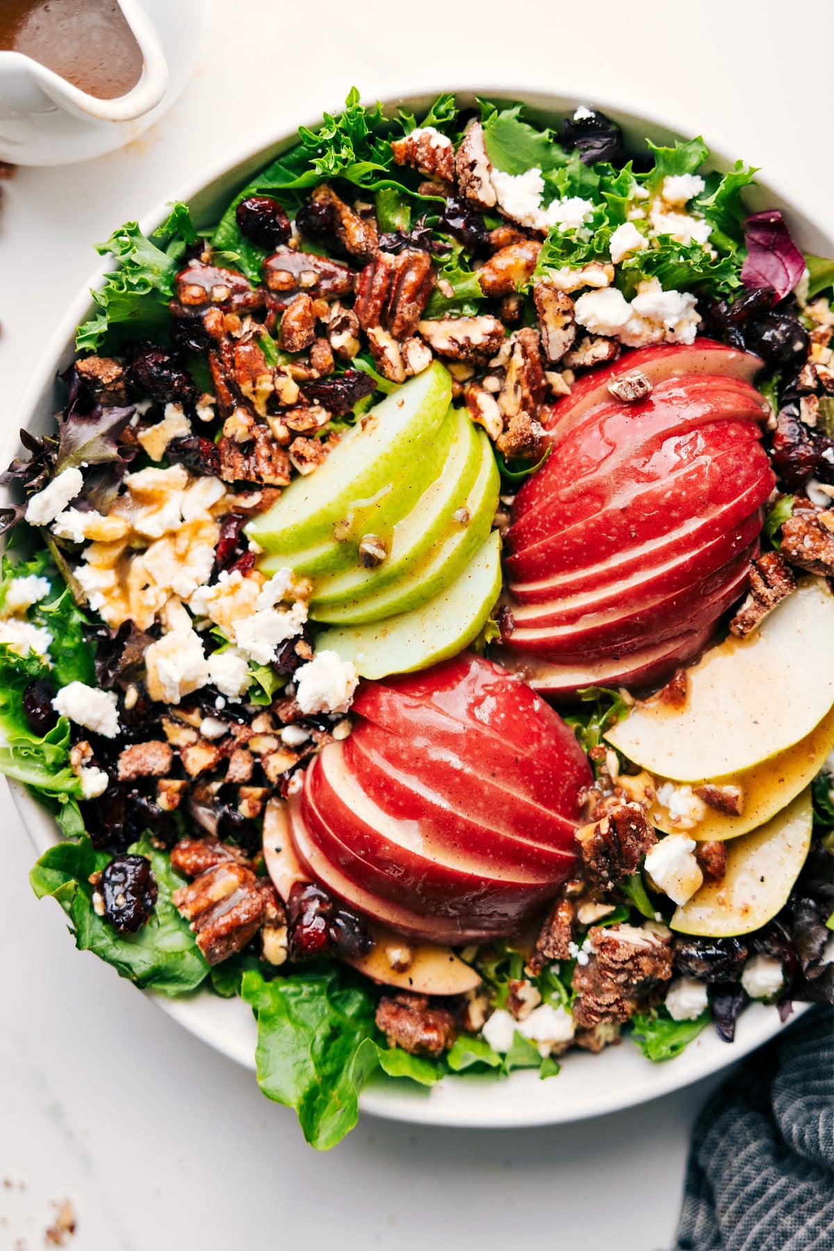 Apple salad recipe in a large bowl, drizzled with dressing before tossing.