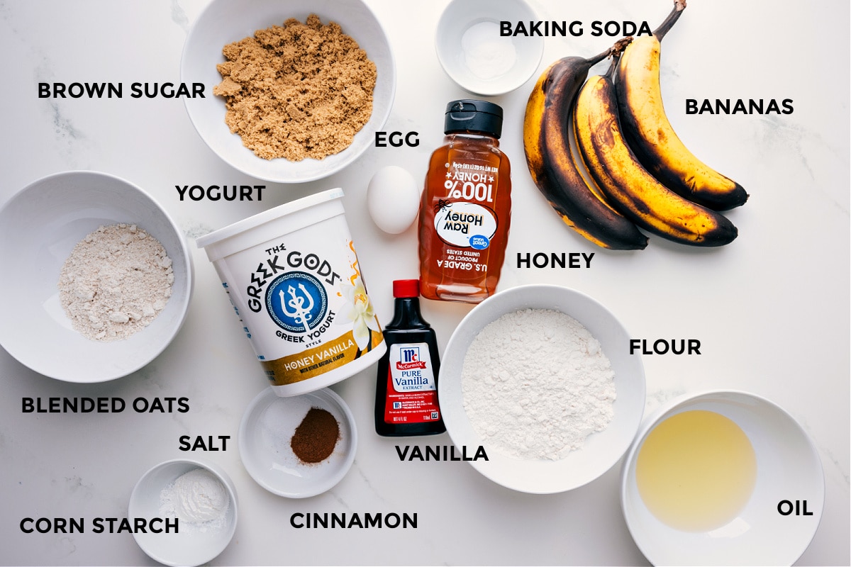 All the ingredients for this recipe prepped and ready for easy assembly, including the fruit, baking soda, egg, brown sugar, honey, yogurt, blended oats, salt, vanilla, cinnamon, flour, and oil.