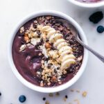 Açaí bowl with almond butter, adorned with various toppings and a spoon on the side, ready to be savored.